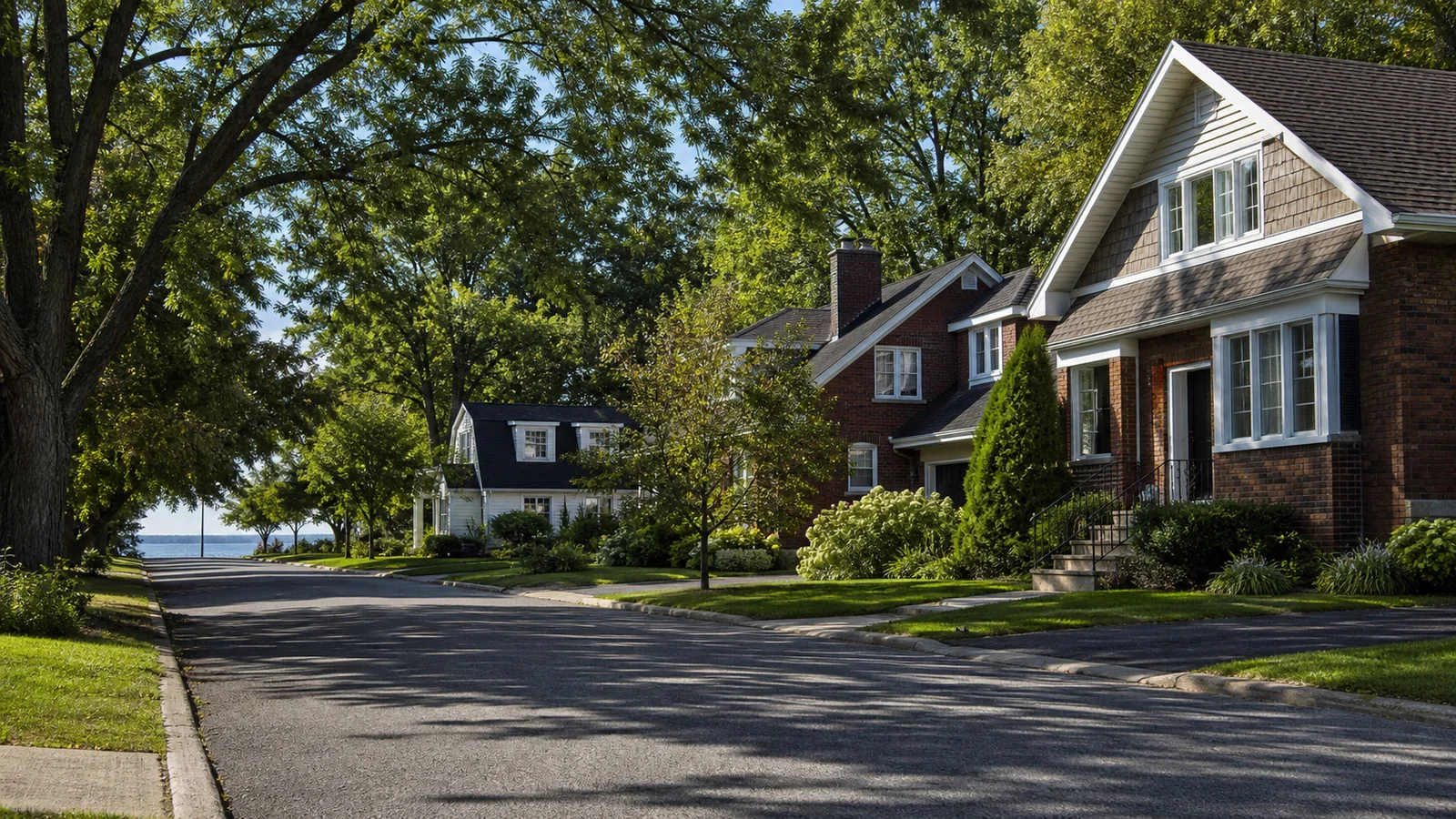 Rue résidentielle arborée de l’Ouest-de-l’Île bordée de maisons familiales près de l’eau.